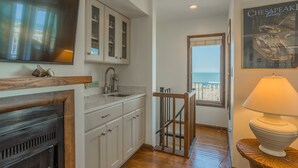 Una cocina con armarios blancos, encimera de madera y un amplio ventanal con vistas a la playa.