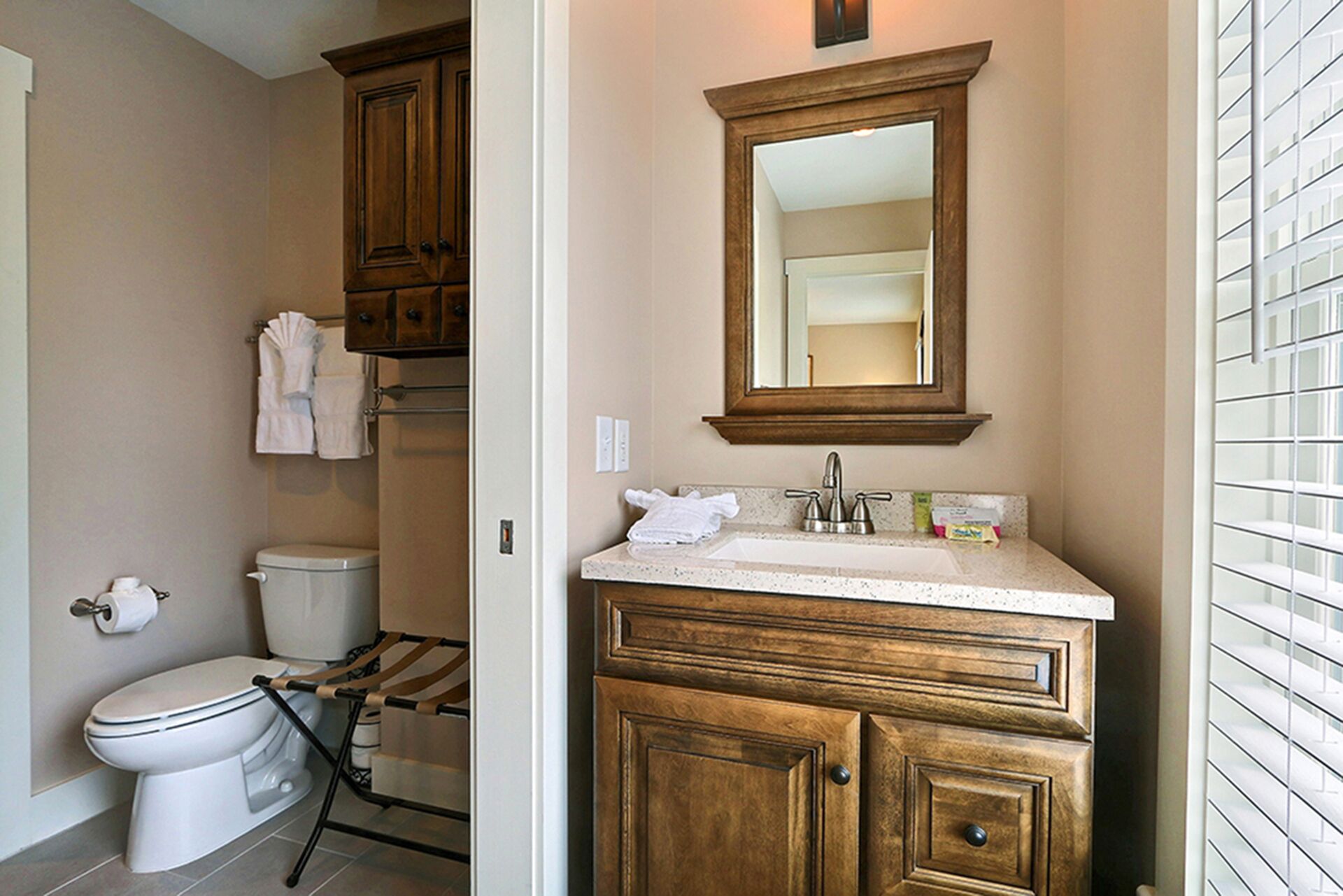 A bathroom with a toilet, a sink with a mirror above it, and wooden cabinets.