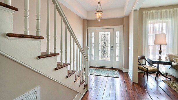 Una escalera con barandillas blancas y escalones de madera que lleva a una puerta con un panel de vidrio decorativo.
