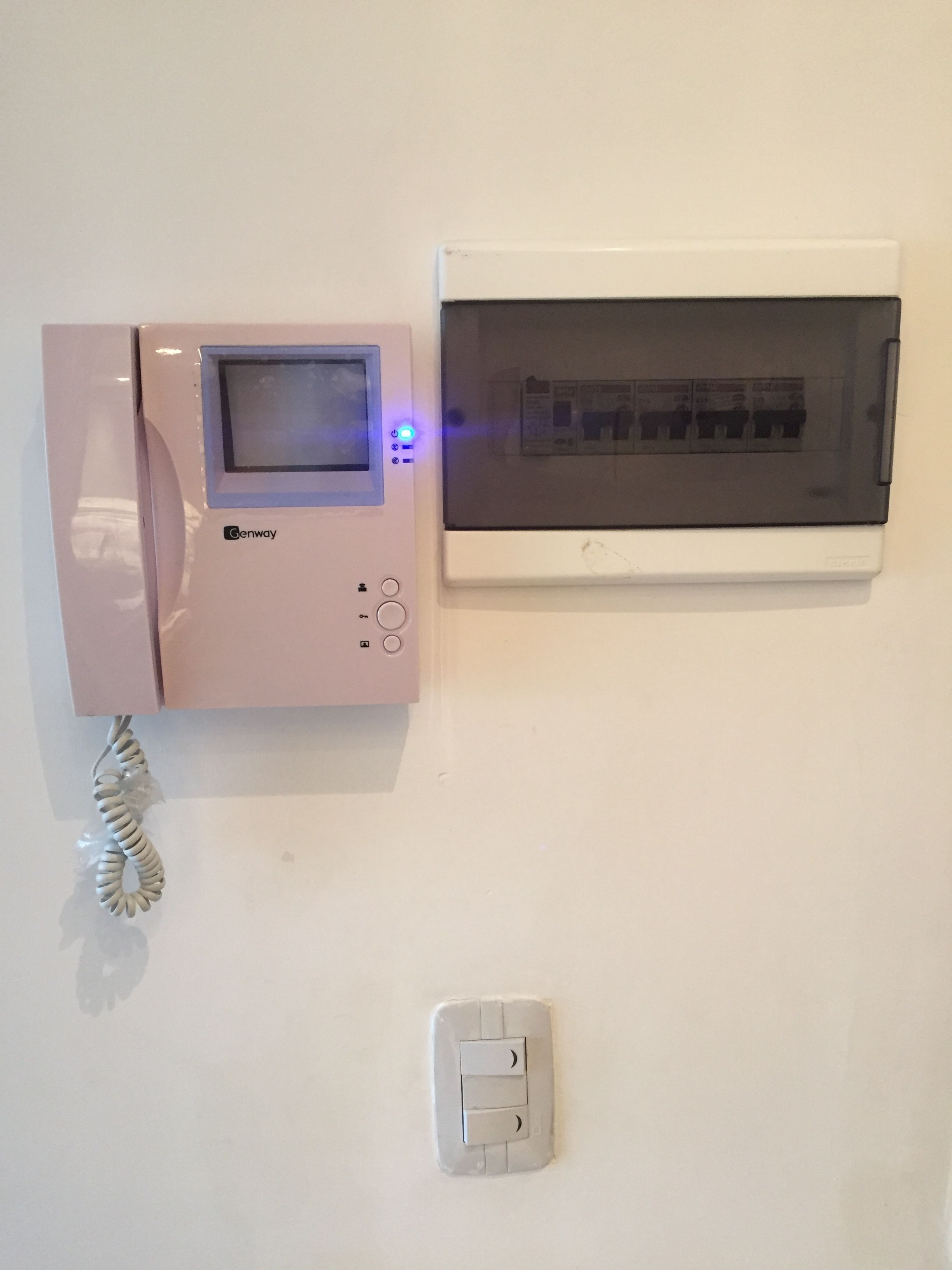 A Genway microwave oven mounted on a white wall, a thermostat, and a light switch.