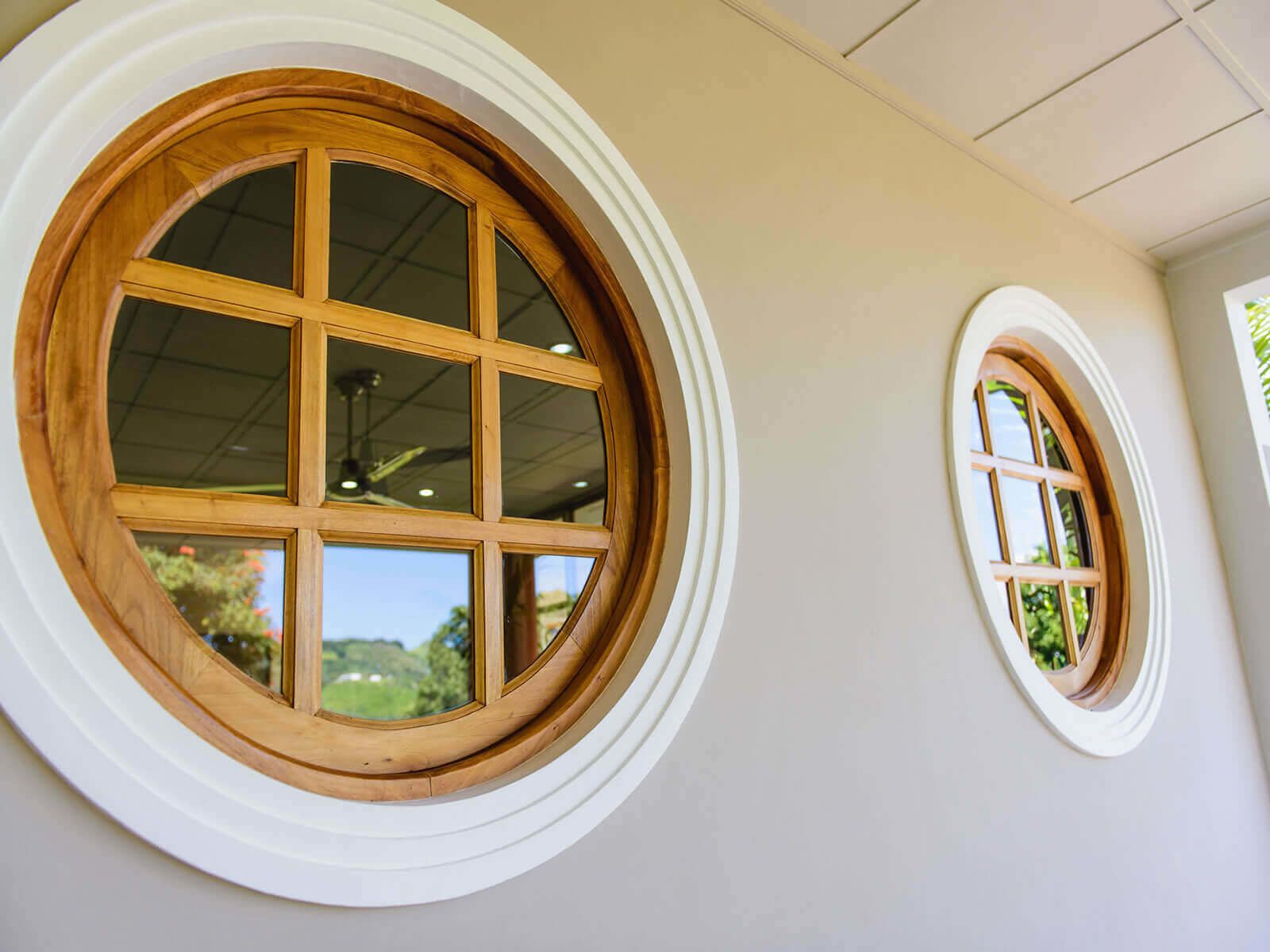 Deux fenêtres rondes, dotées de cadres en bois et de bordures blanches, qui font partie de la façade d’un bâtiment.