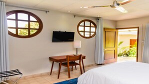 Et hotelværelse med en seng, et skrivebord med stol, et fjernsyn ophængt på væggen og en dør, der fører til et udendørs område.