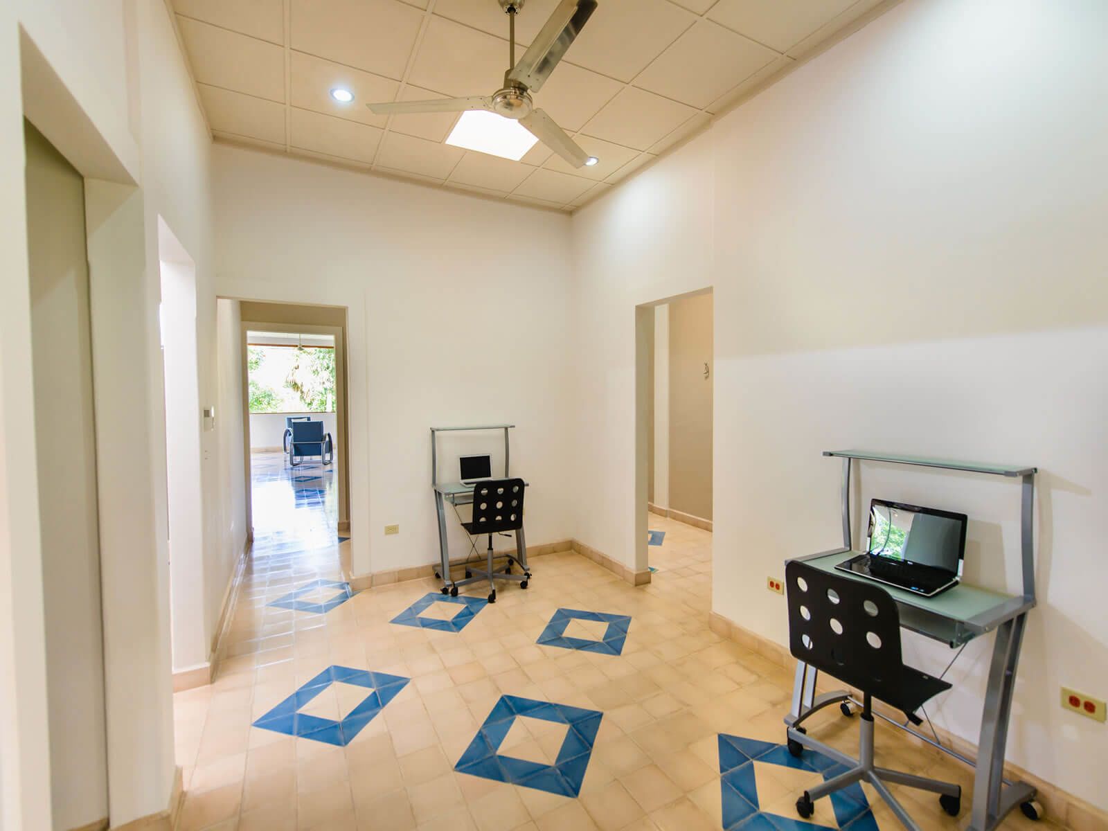 A spacious room with a ceiling fan, a desk with a laptop, and a chair.