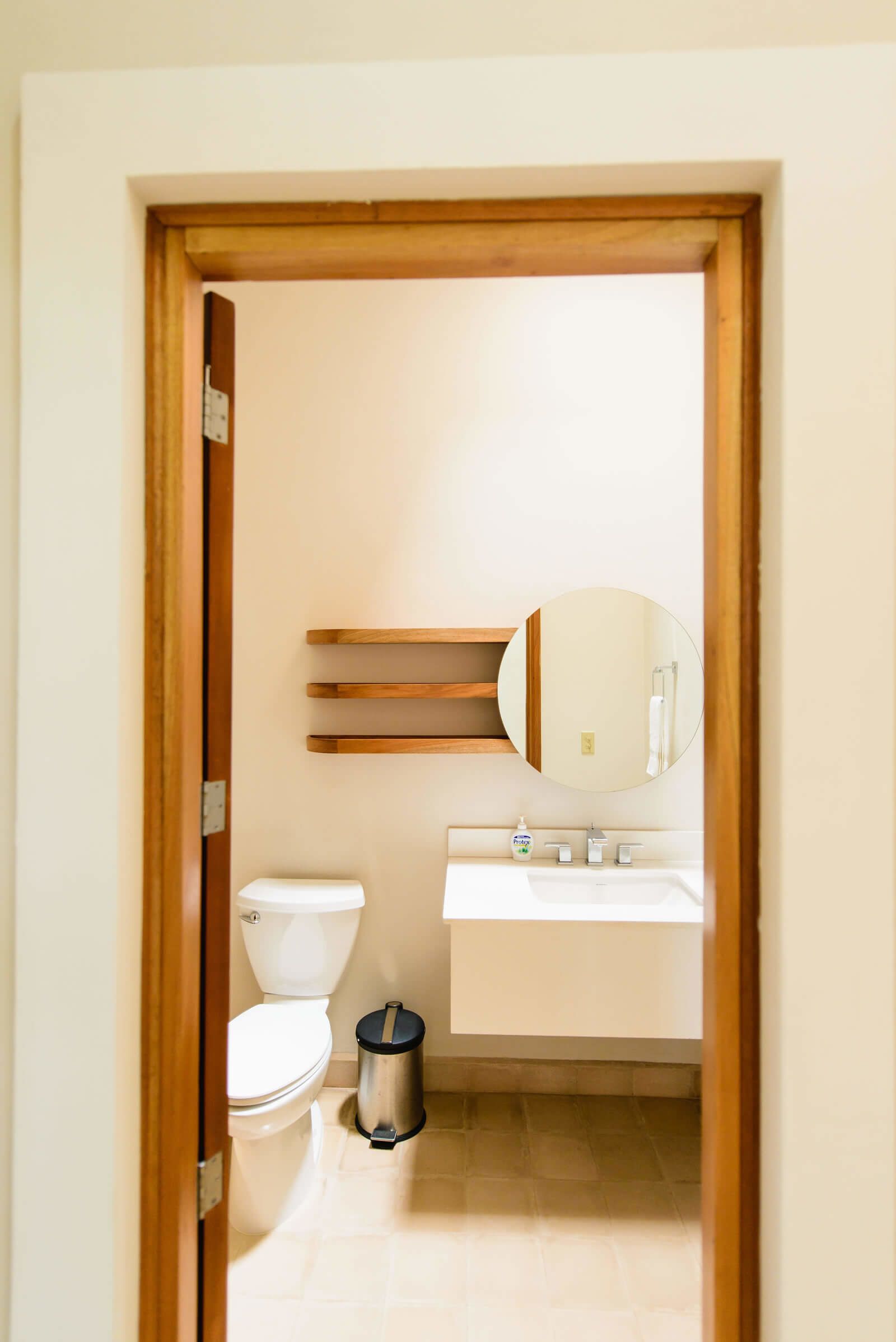 A bathroom with a toilet, sink, mirror, and trash bin.