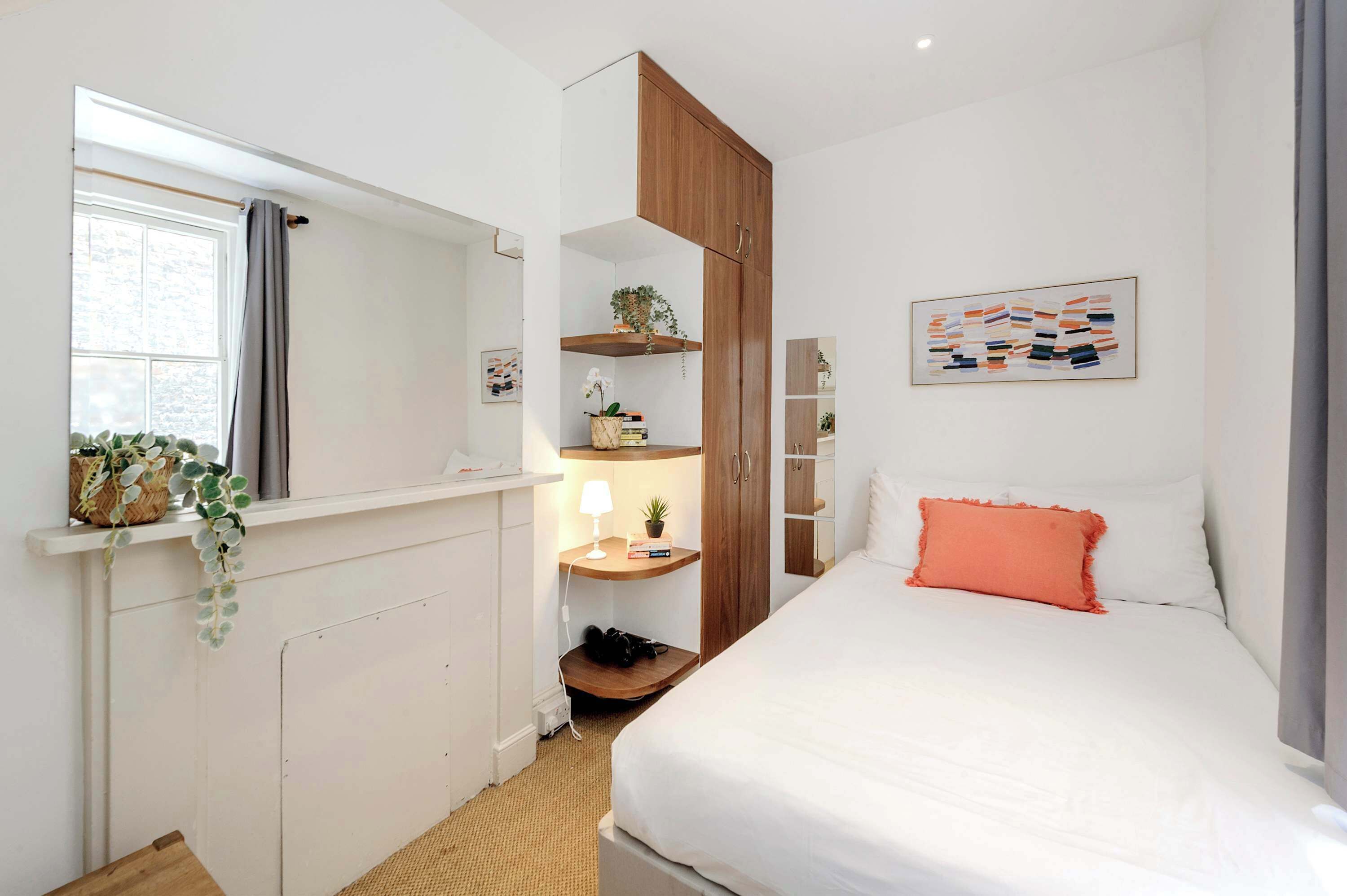 Ein Schlafzimmer mit Bett, Schrank, Nachttisch mit Lampe und Fenster mit Vorhängen.
