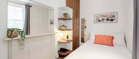Ein Schlafzimmer mit Bett, Schrank, Nachttisch mit Lampe und Fenster mit Vorhängen.