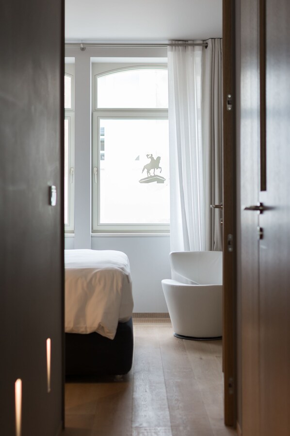 Un dormitorio con cama, una bañera blanca y una ventana con cortinas.