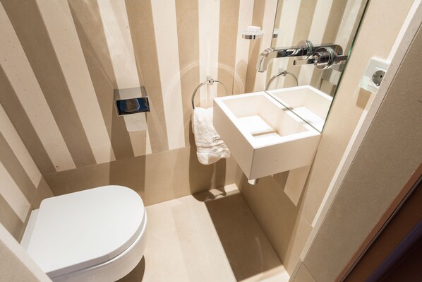 A small, modern bathroom with a white toilet, a sink, and a mirror. - Guillaume Suites (Luxembourg City)