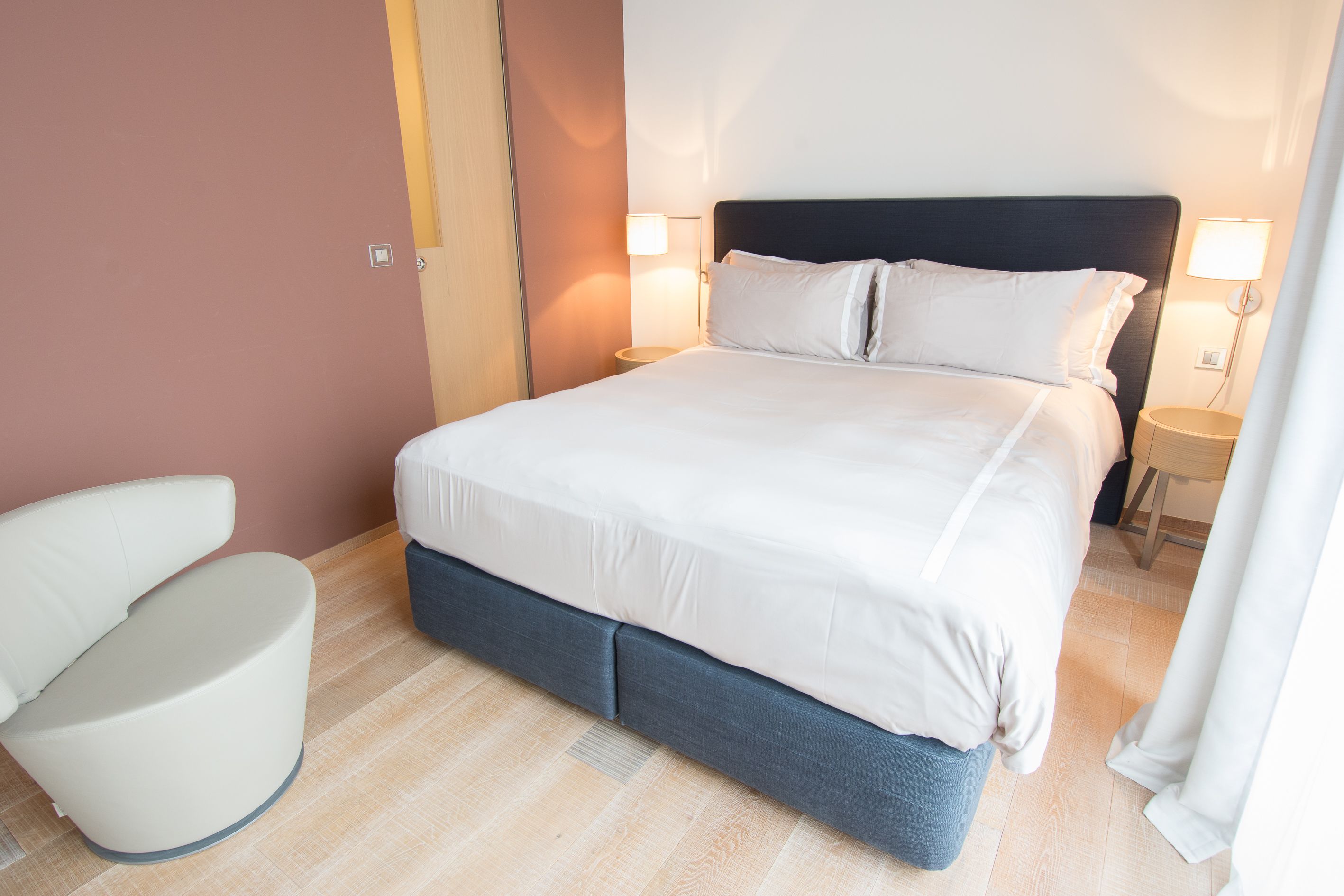 A neatly made bed with white linens, a dark headboard, and two bedside lamps.