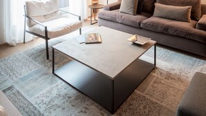 A modern living room with a sofa, armchair, and coffee table. There is a bookshelf and a lamp.