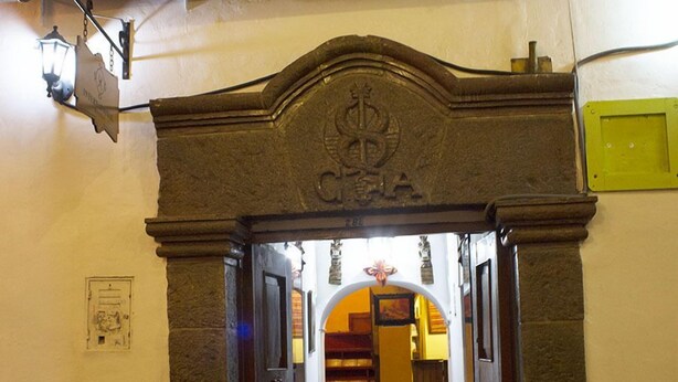 Una entrada con un arco de piedra, una campana y una escalera que conduce al interior.