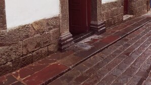 Una estrecha calle adoquinada con un edificio de piedra, una puerta de madera y un pequeño ventanal.