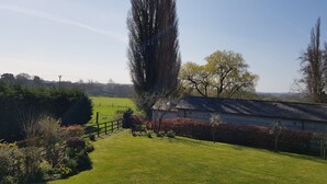 Ländliche Landschaft mit einem großen Baum, einem Holzzaun und einem Gebäude mit geneigtem Dach.