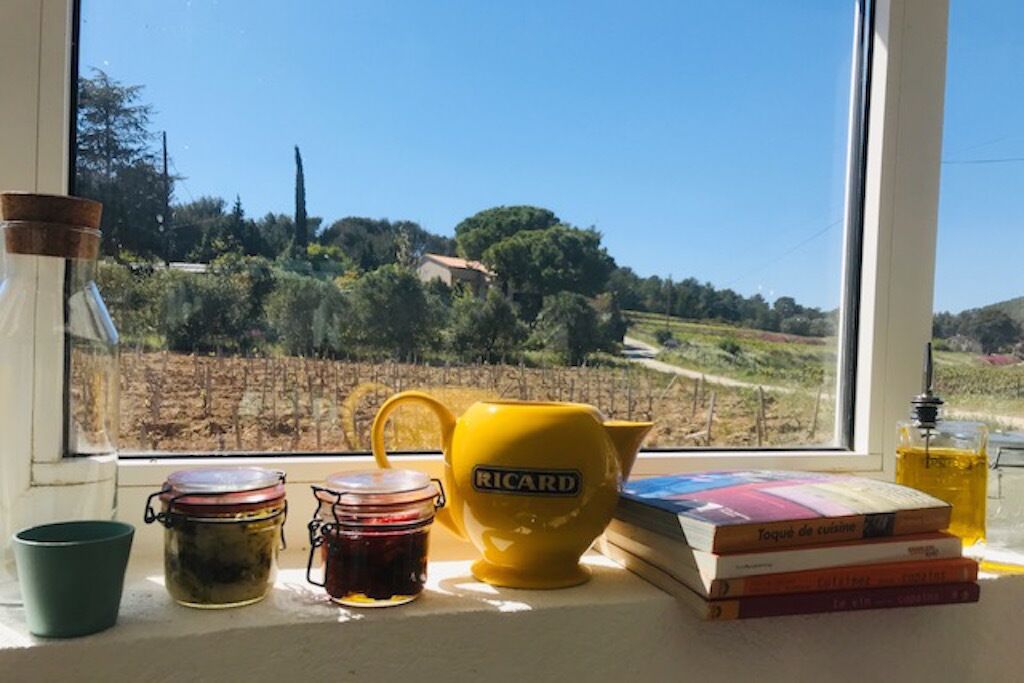 Blick aus dem Fenster auf einen Weinberg, eine gelbe Teekanne, Gläser und Bücher auf einem Fensterbrett.