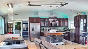 A spacious living area with a large sectional sofa, a dining table with bar stools, a kitchen with dark cabinets, and a ceiling fan. - Private Luxury Pool / Swim up bar / Smart-home (Orlando)