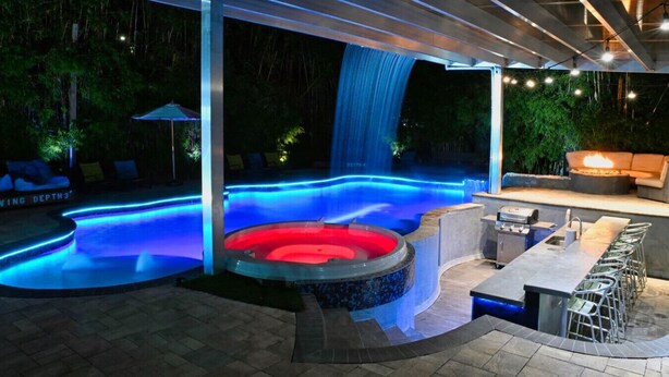 A hot tub with a waterfall feature, a covered seating area, and a bar with outdoor seating. - Private Luxury Pool / Swim up bar / Smart-home (Orlando)