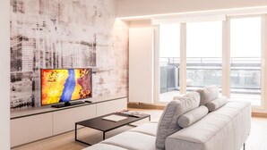 Un salon moderne doté d’un grand téléviseur à écran plat, d’un canapé gris, d’une table basse et d’une œuvre d’art représentant un paysage urbain accrochée au mur.