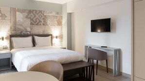 Une chambre d’hôtel moderne, dotée d’un grand lit, d’un bureau, d’une chaise et d’un téléviseur à écran plat fixé au mur.