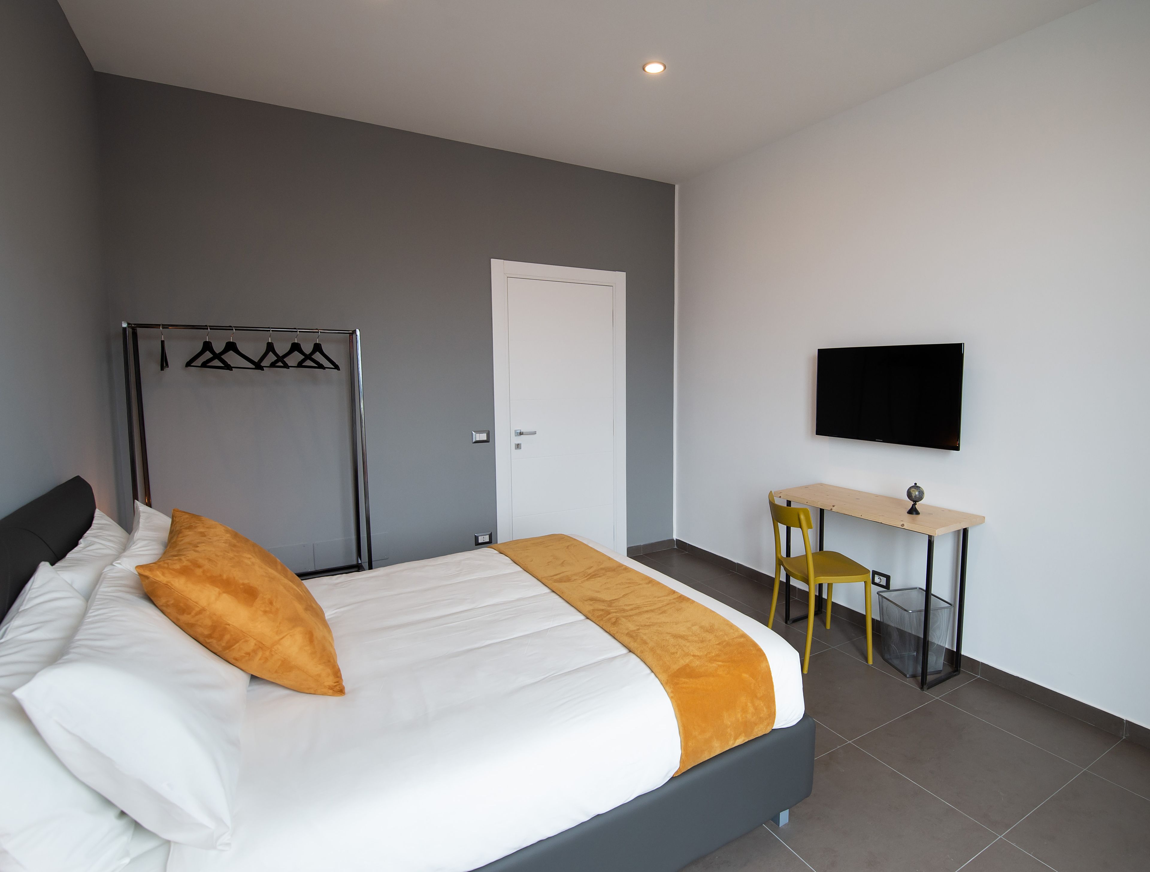 A modern hotel room with a bed, a desk, a chair, a TV, and a wardrobe.