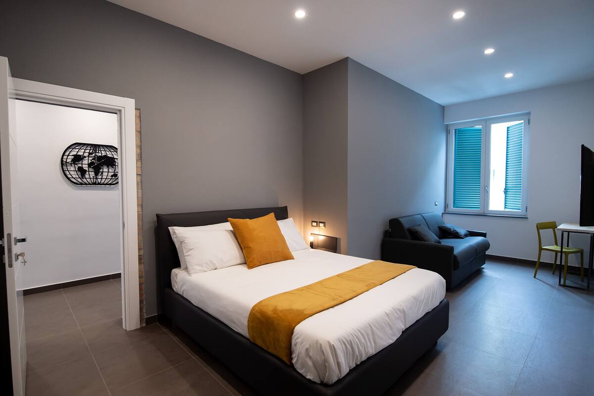 A modern bedroom with a bed, a sofa, a chair, and a desk.