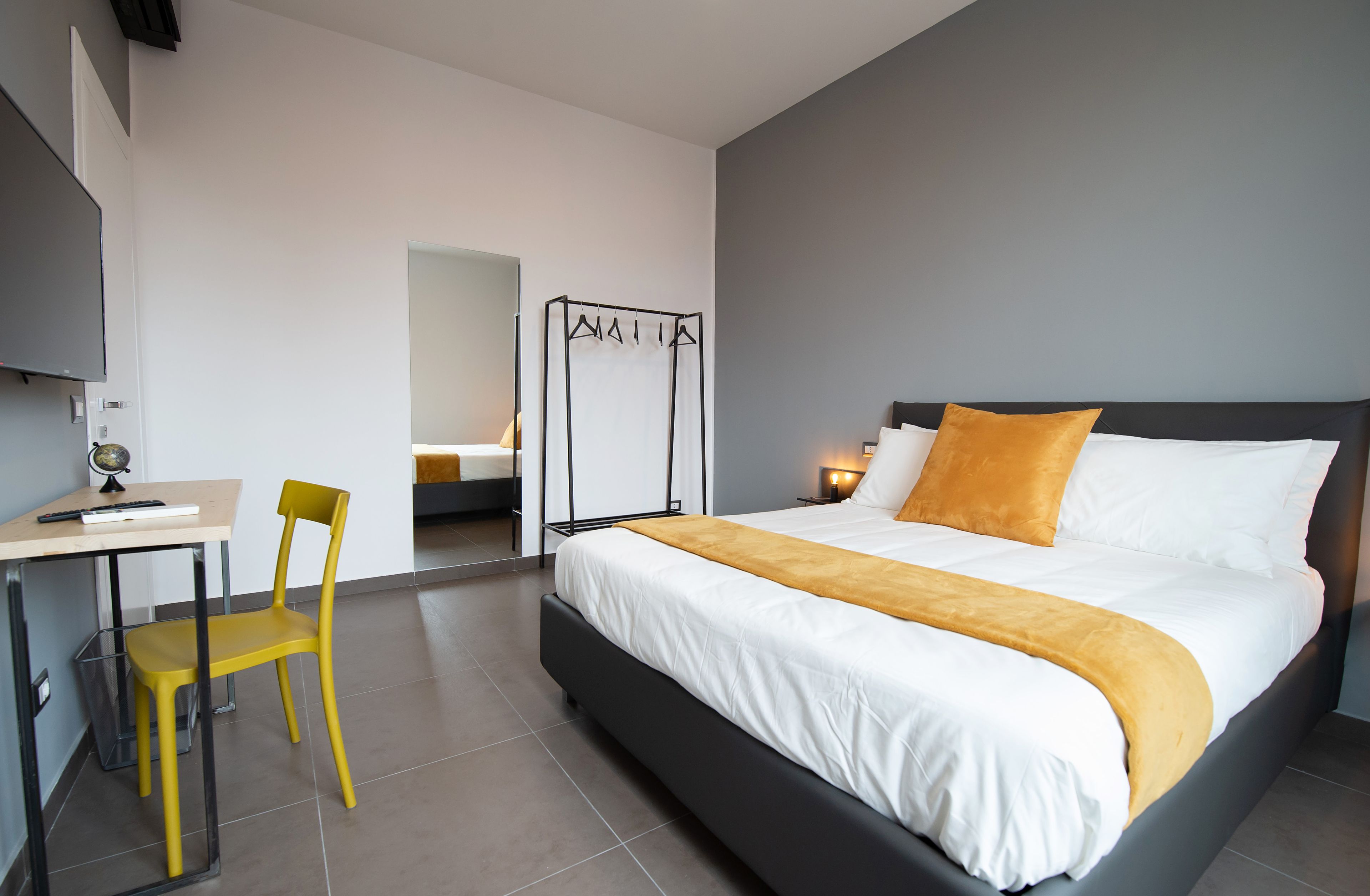 A modern hotel room with a large bed, a desk with a chair, and a coat rack.