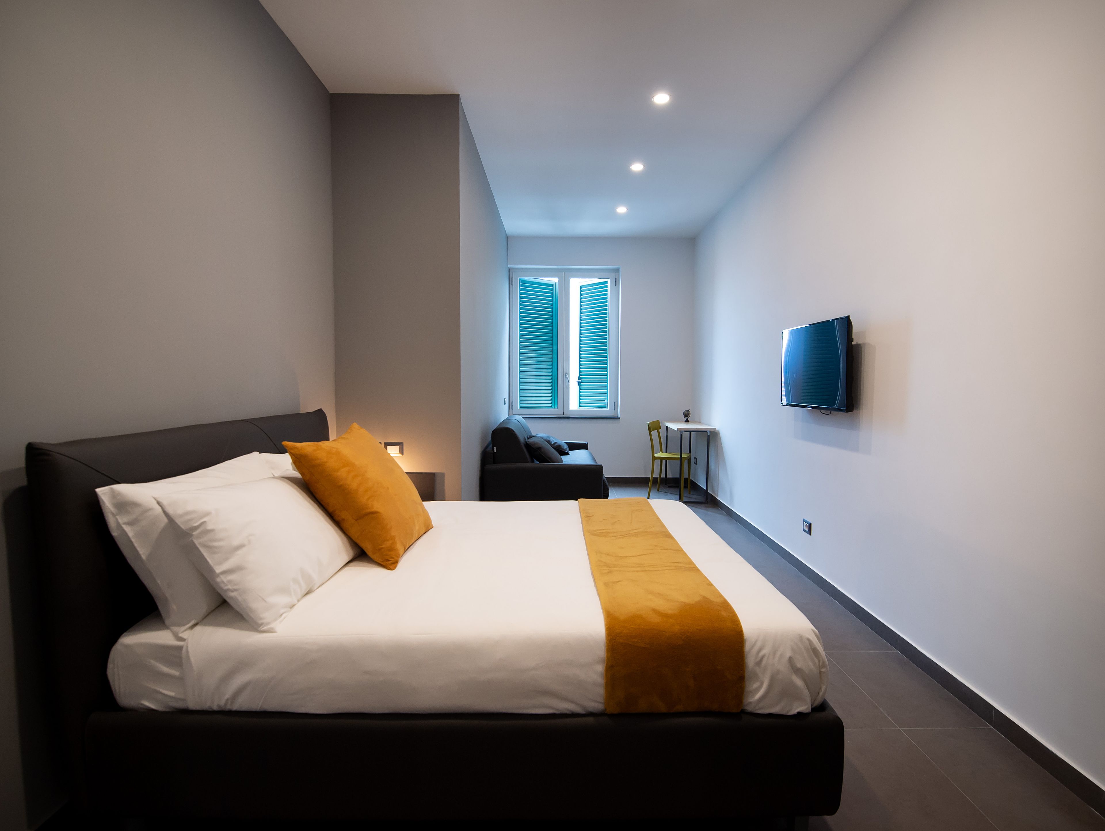 A modern hotel room with a large bed, a small desk, and a television on the wall.