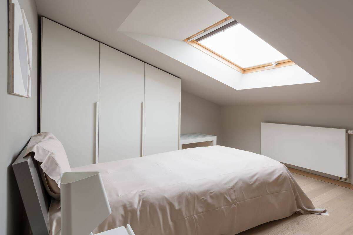 A bedroom with a skylight, a bed, a wardrobe, and a radiator.