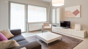 A modern living room with a sofa, coffee table, and a TV on a white cabinet. - Four Stars Aparthotel (Luxembourg City)