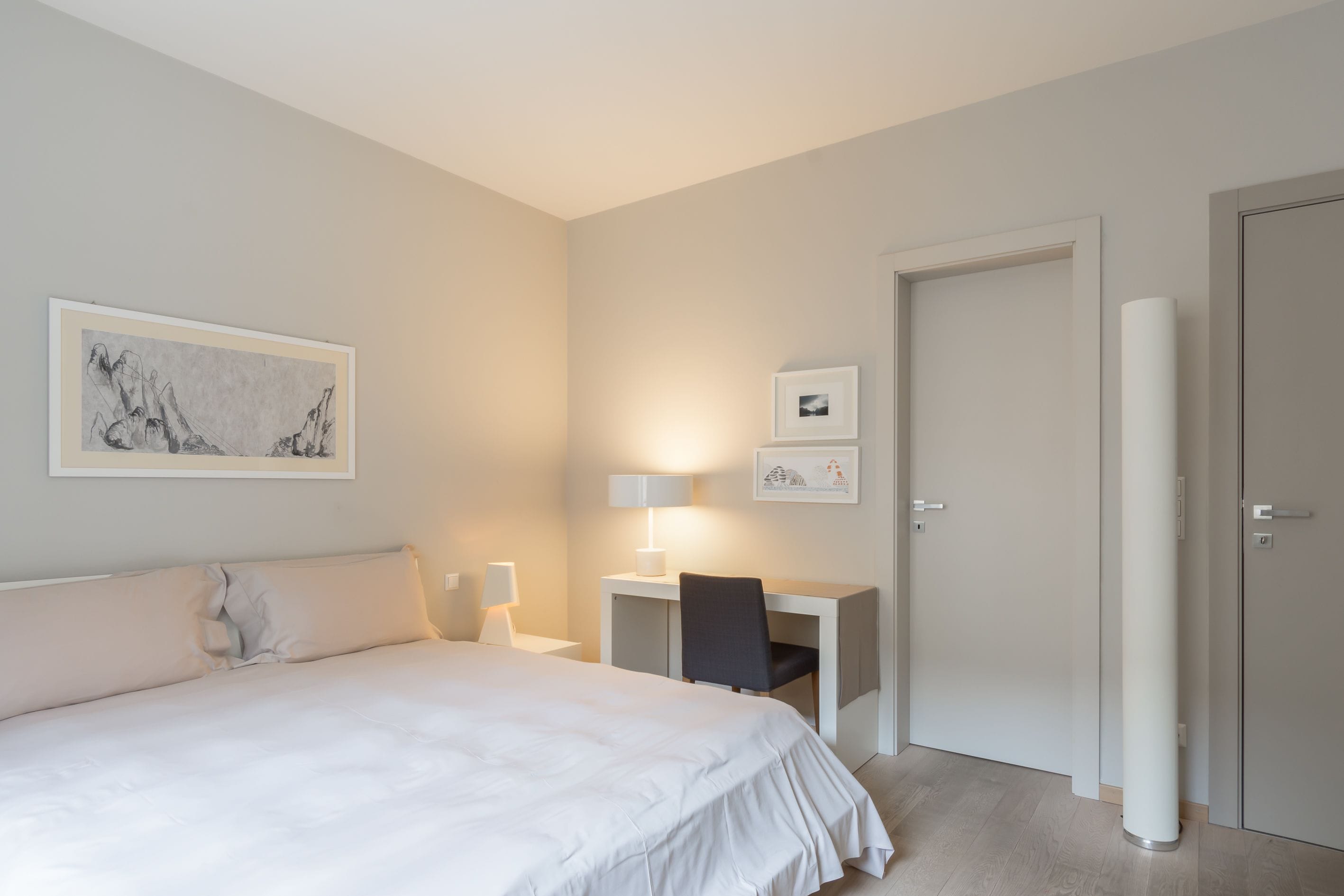 A bedroom with a large bed, a desk, and a chair. There are two bedside tables with lamps.