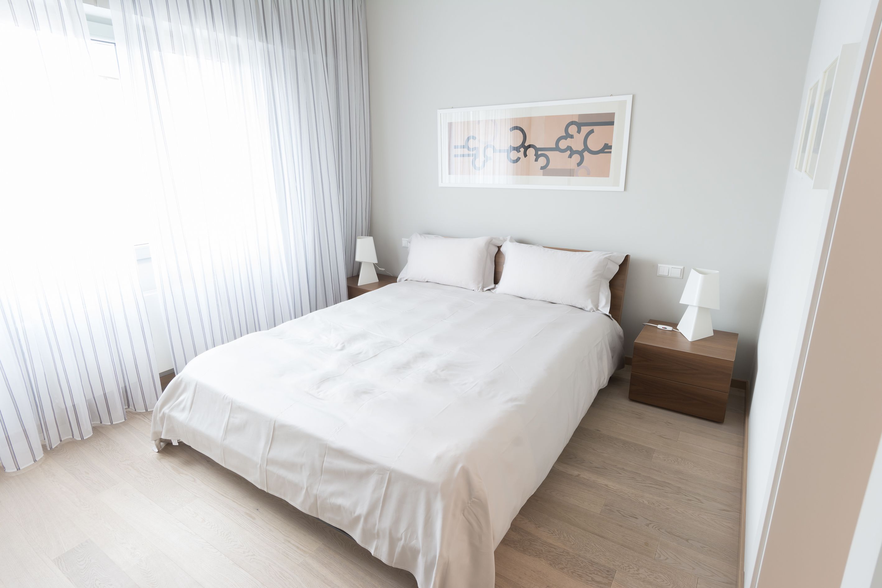A neatly made bed with white linens, a wooden nightstand with a lamp, and a framed artwork on the wall.