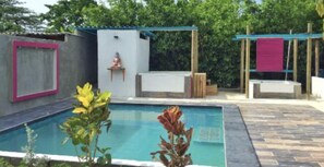 Ein Schwimmbecken mit einer kleinen Buddha-Statue, einem überdachten Sitzbereich und einem Holzdeck.
