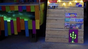Eine Holzkonstruktion mit farbigen, senkrechten Lamellen und einer Kaktus-Lampenleuchte.