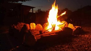 A campfire with logs and rocks, surrounded by a gravel area, with a building in the background. - Paraiso Lounge Santa Marta (Santa Marta)