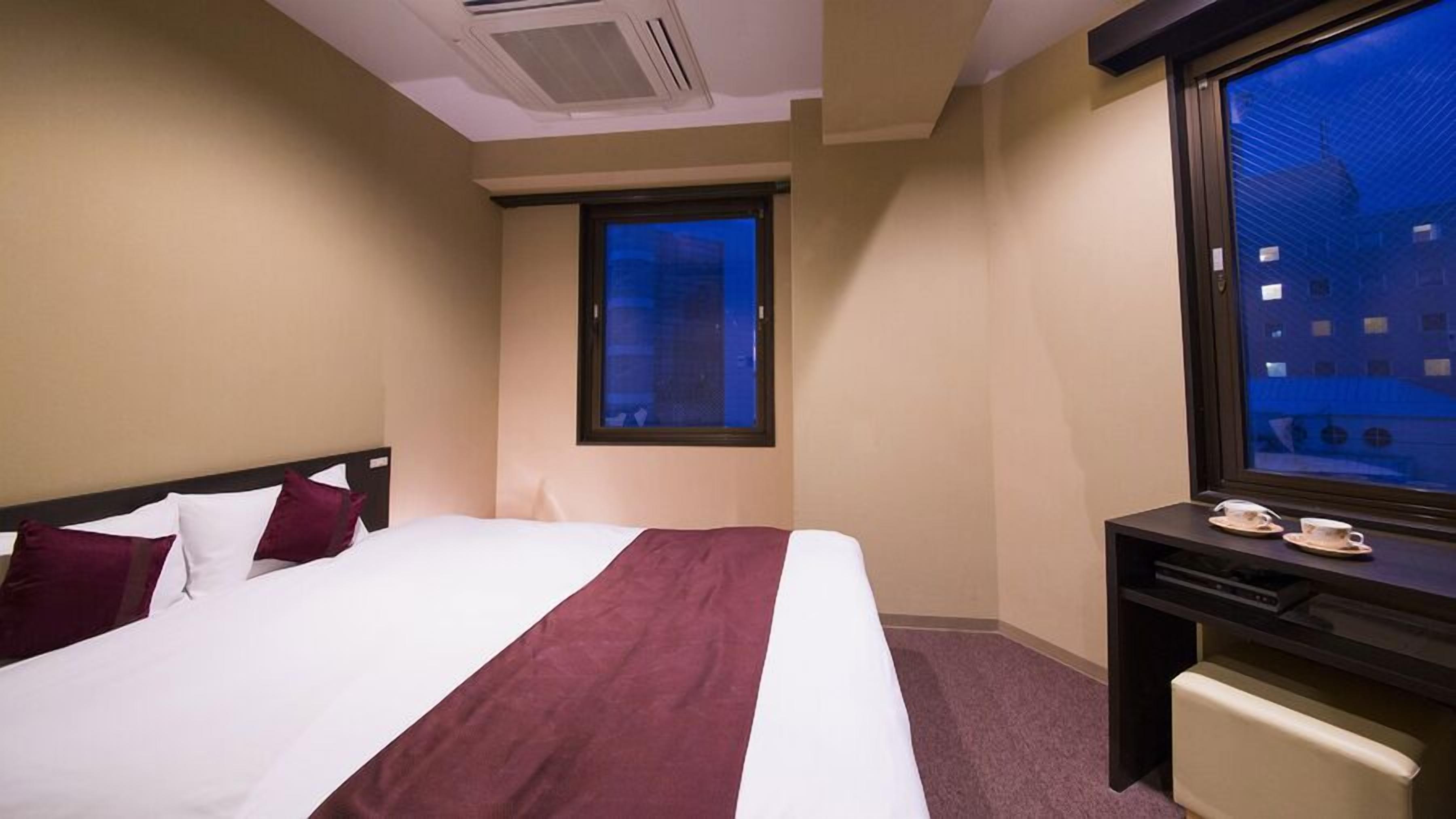 Habitación de hotel con cama, escritorio, ventana y vista a edificios.