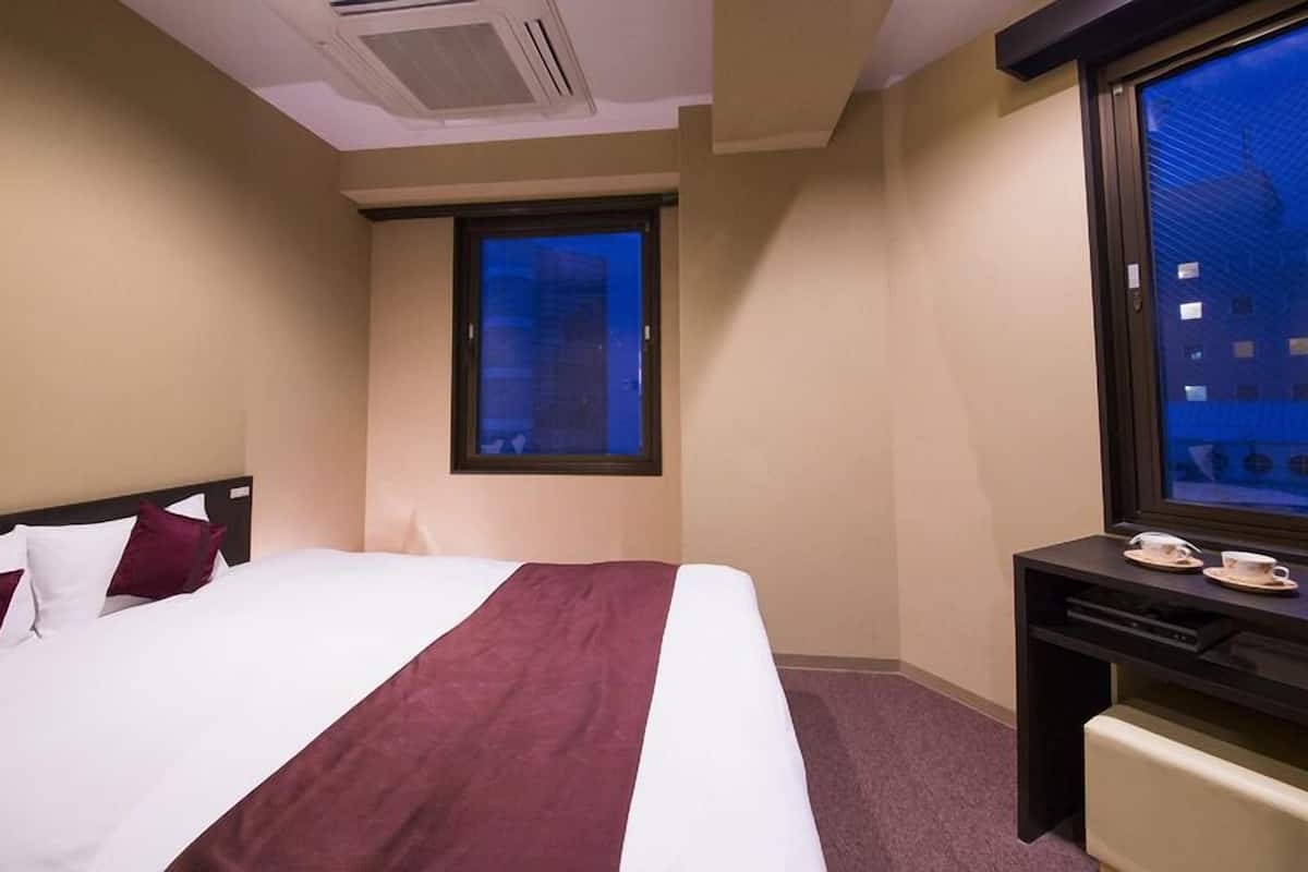 Habitación de hotel con cama, escritorio, ventana y vista a edificios.