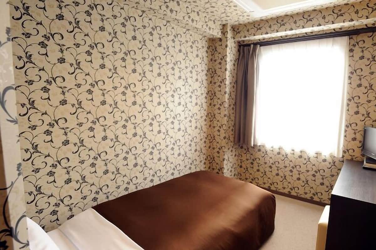 Une chambre d’hôtel avec un papier peint à motifs floraux, un lit, un bureau avec une lampe et un téléviseur.