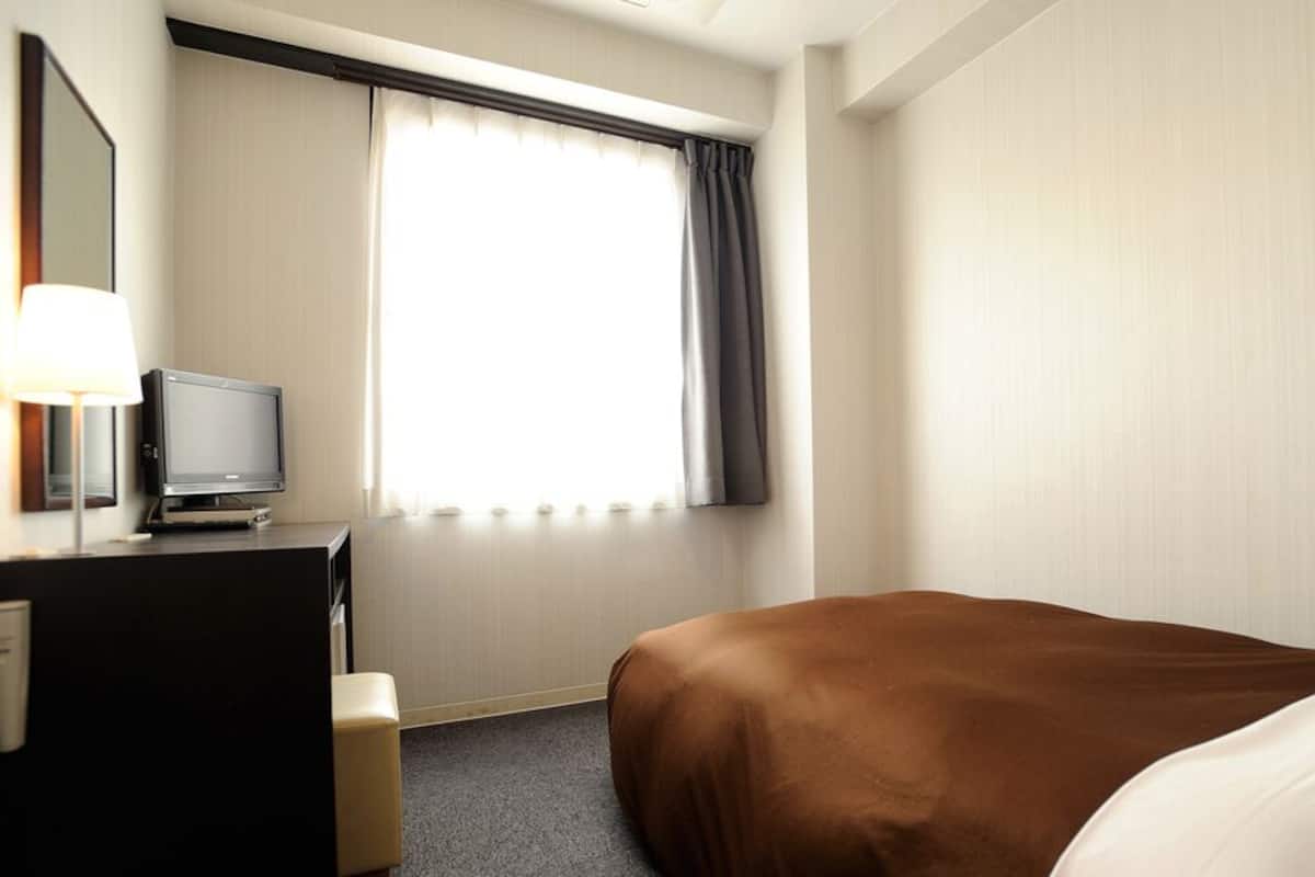 Une chambre d’hôtel avec un lit, un bureau, une télévision et une fenêtre avec des rideaux.