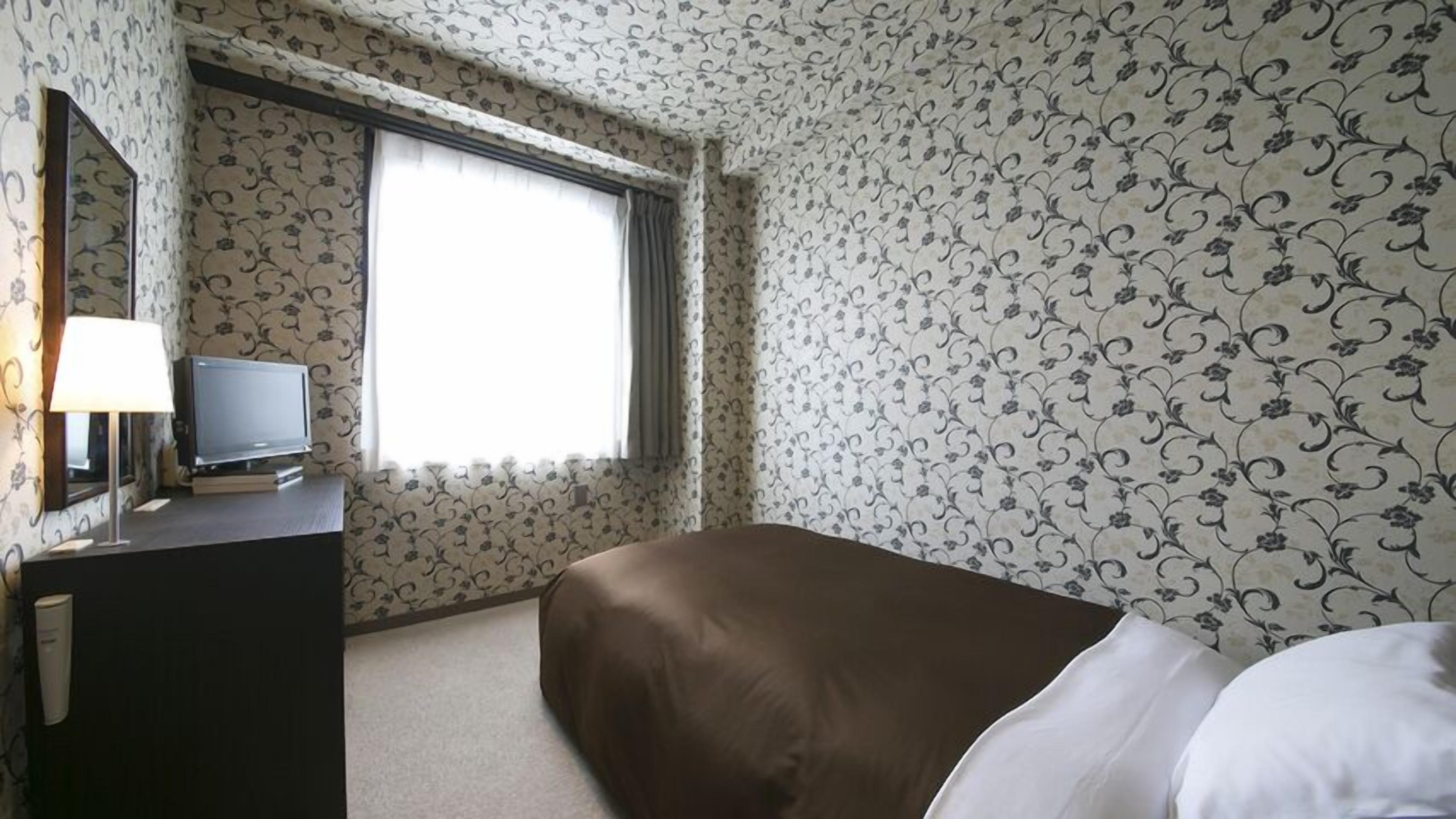 Una habitación de hotel con cama, televisor en una cómoda y ventana con cortinas.