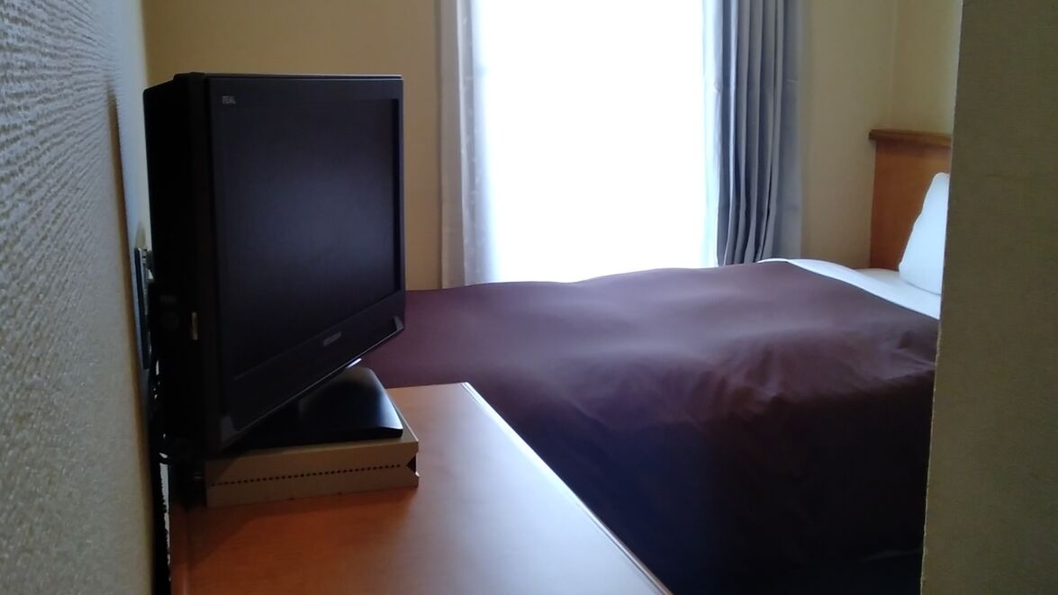 Una habitación de hotel con una cama, un televisor sobre un mueble y una ventana con cortinas.