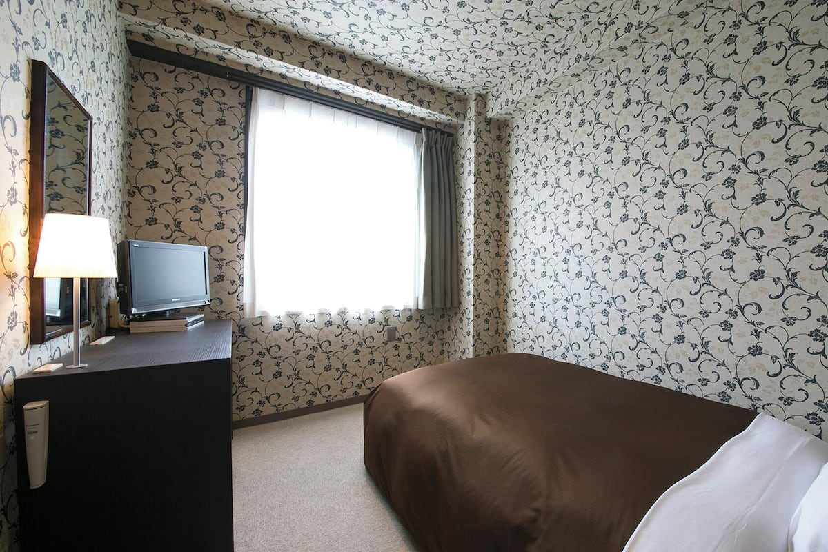 Une chambre d’hôtel avec un lit, un téléviseur posé sur une commode et une fenêtre avec des rideaux.