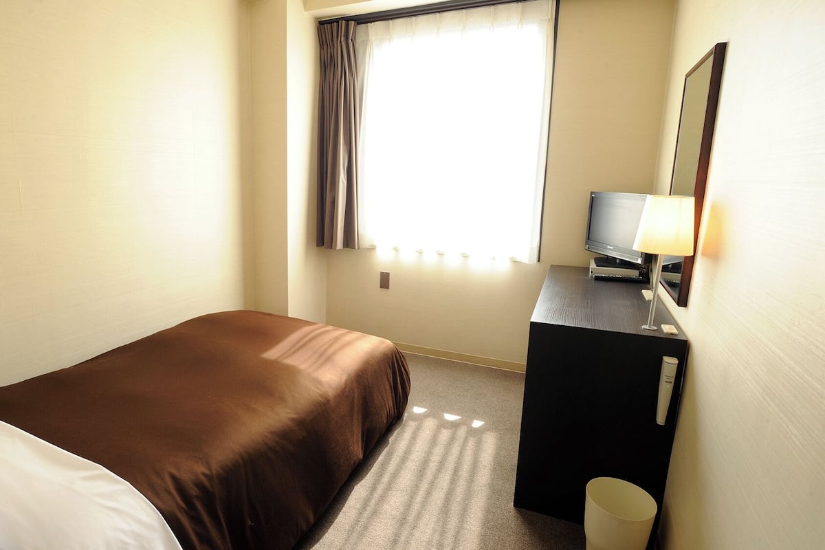 A hotel room with a bed, a desk with a TV, a lamp, and a mirror.