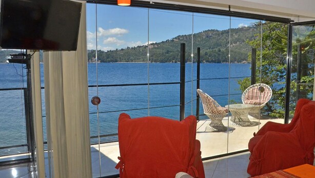 Een balkon met uitzicht op een meer, rieten stoelen en een tafel.