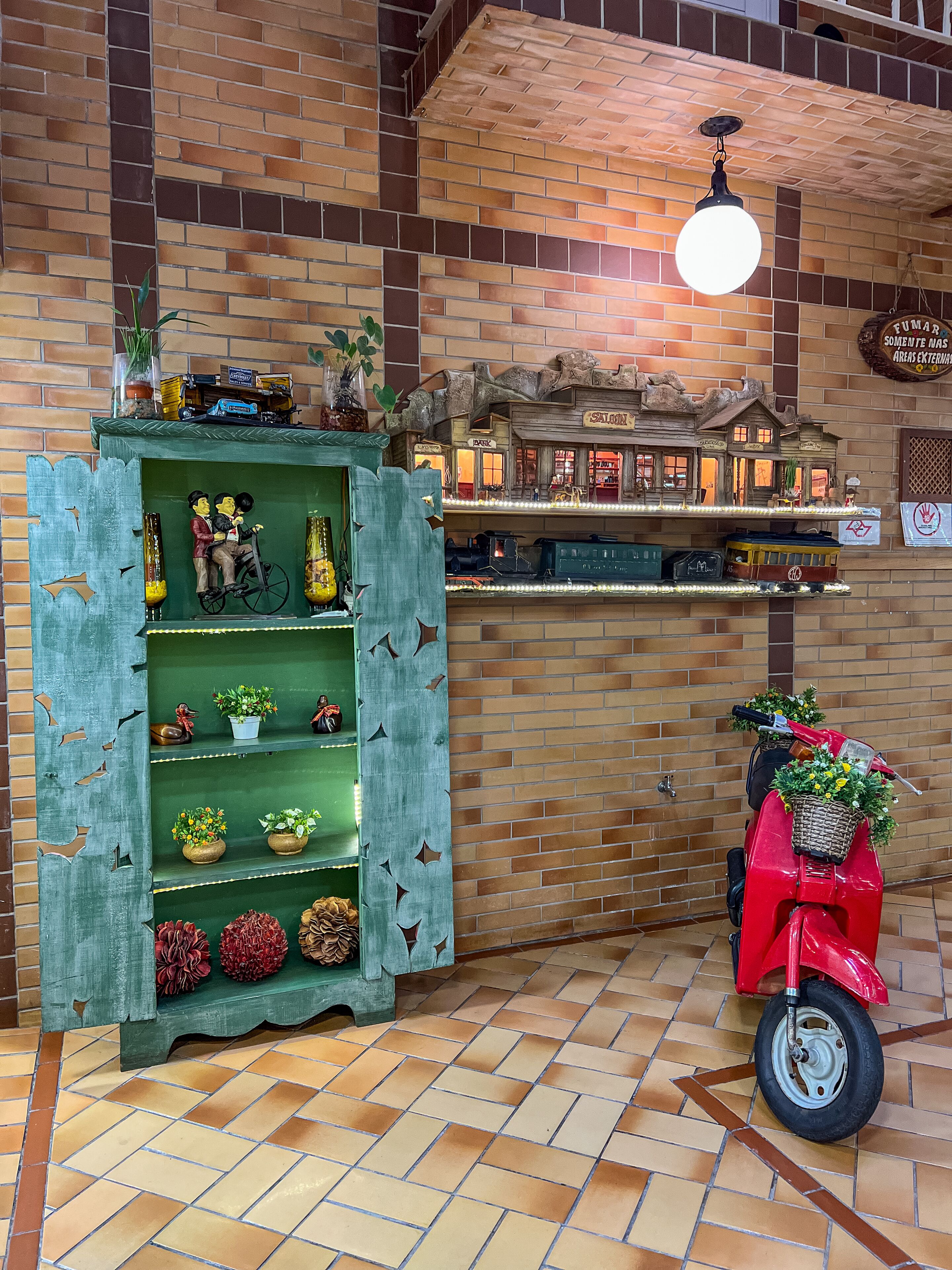 A model train display with a brick wall backdrop and a red scooter with a basket of flowers.