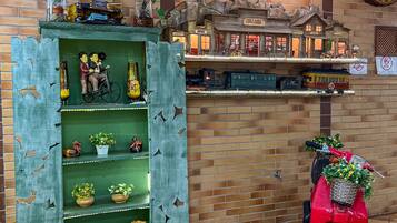 A model train display with a brick wall backdrop and a red scooter with a basket of flowers.