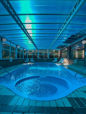 Piscina interior com hidromassagem, rodeada por espreguiçadeiras e uma área coberta com telhado azul.