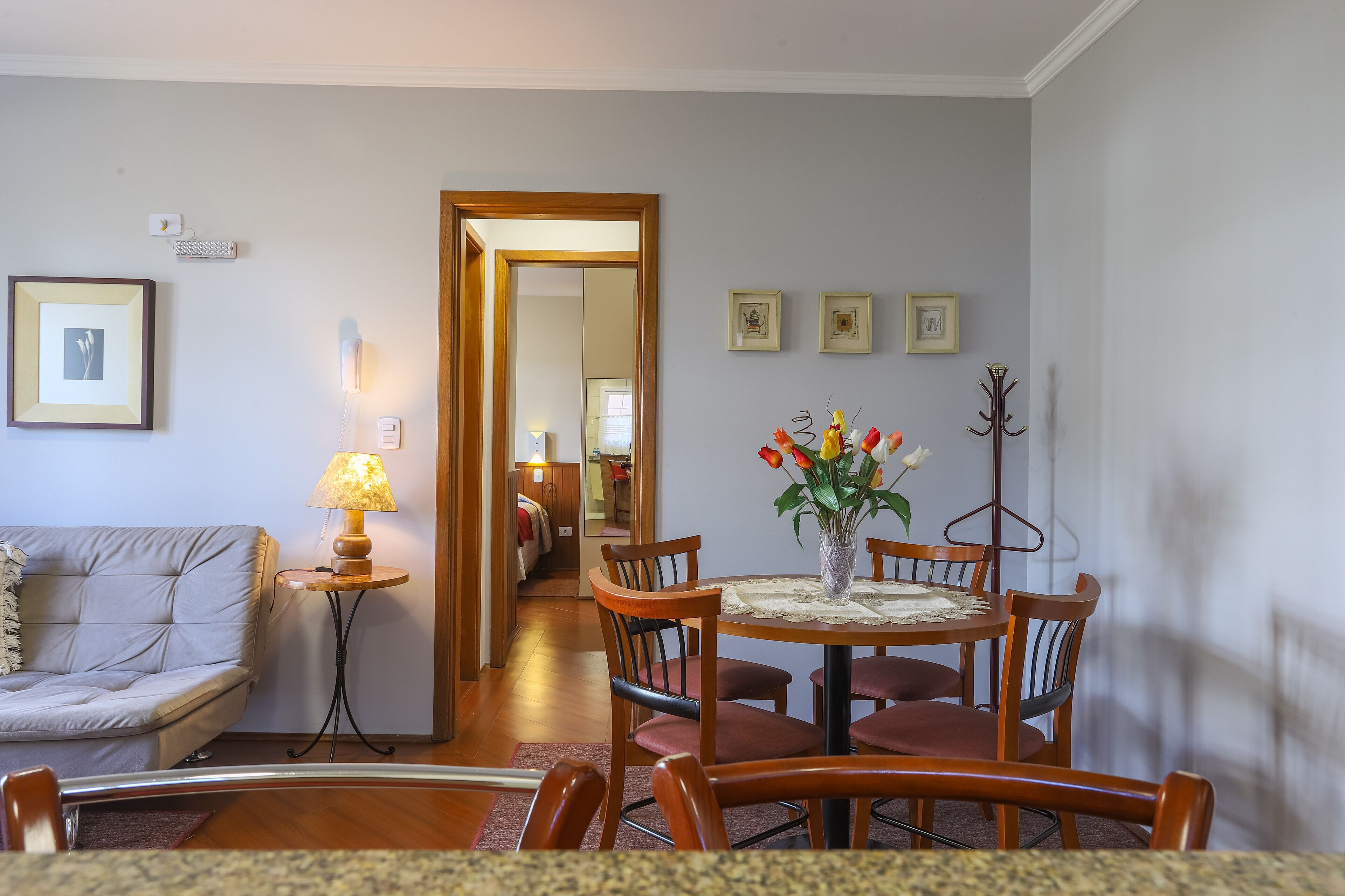 A dining area with a round table, chairs, a vase with flowers, a lamp, and a coat rack.