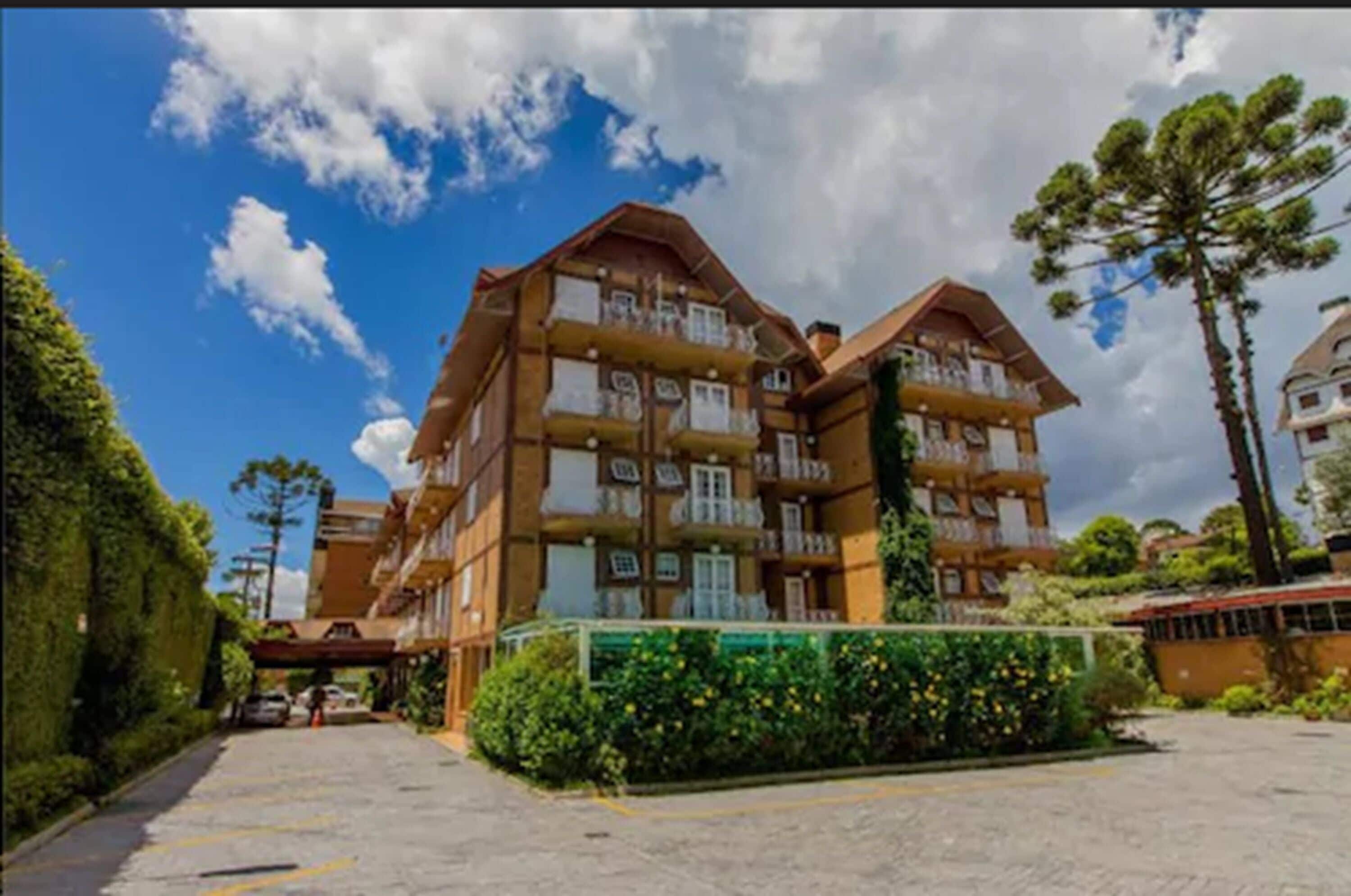 A multi-story hotel with balconies, a parking area, and surrounding greenery.