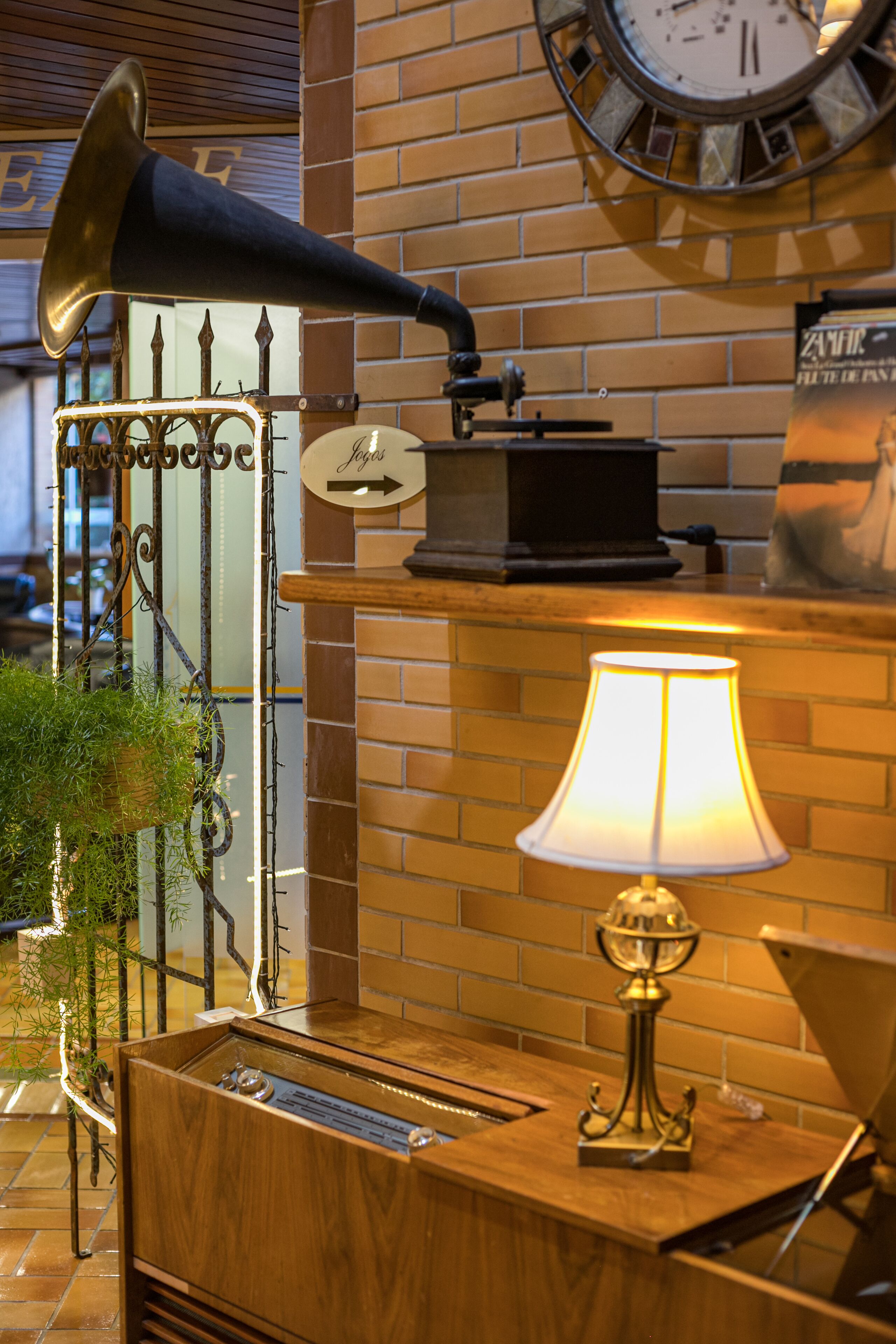 A vintage radio, a clock, and a lamp on a wooden counter against a brick wall.