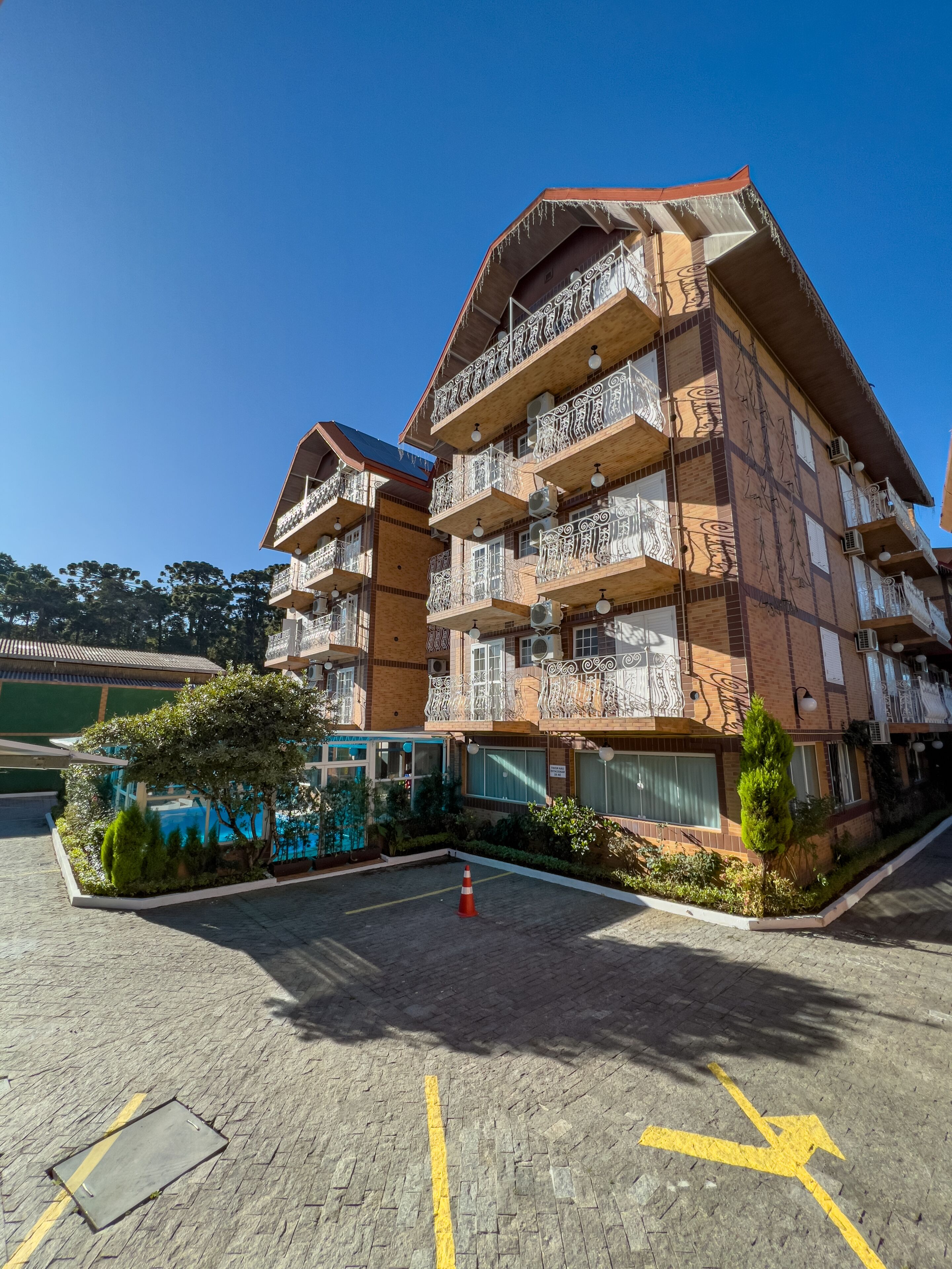 A multi-story hotel with balconies, a parking area, and a small garden.