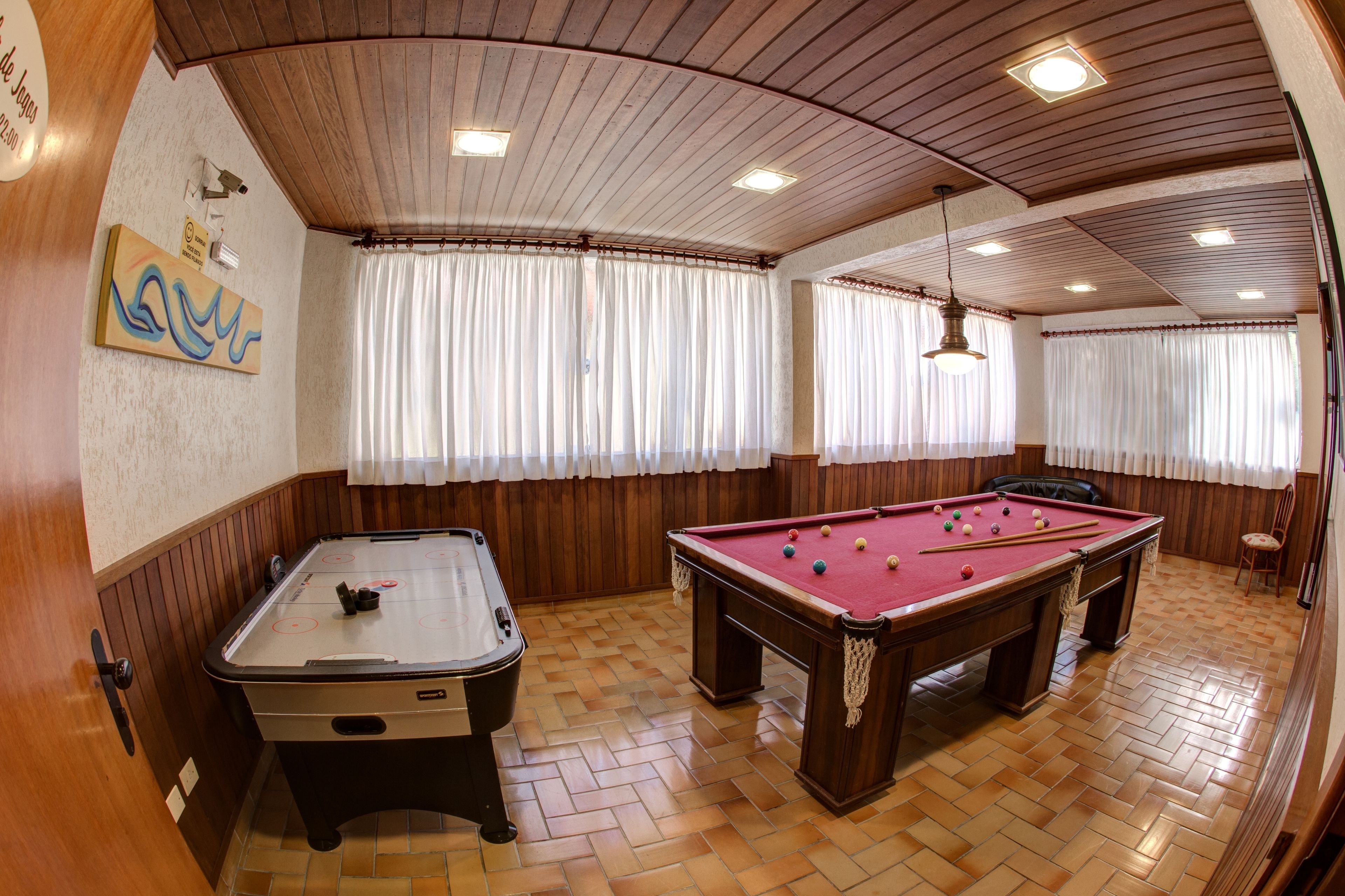 A pool table in a room with wooden paneling, a foosball table, and a billiards table.